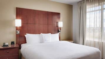 Habitación de hotel con una cama grande, dos mesitas de noche, cabecera de madera y una ventana con cortinas traslúcidas.