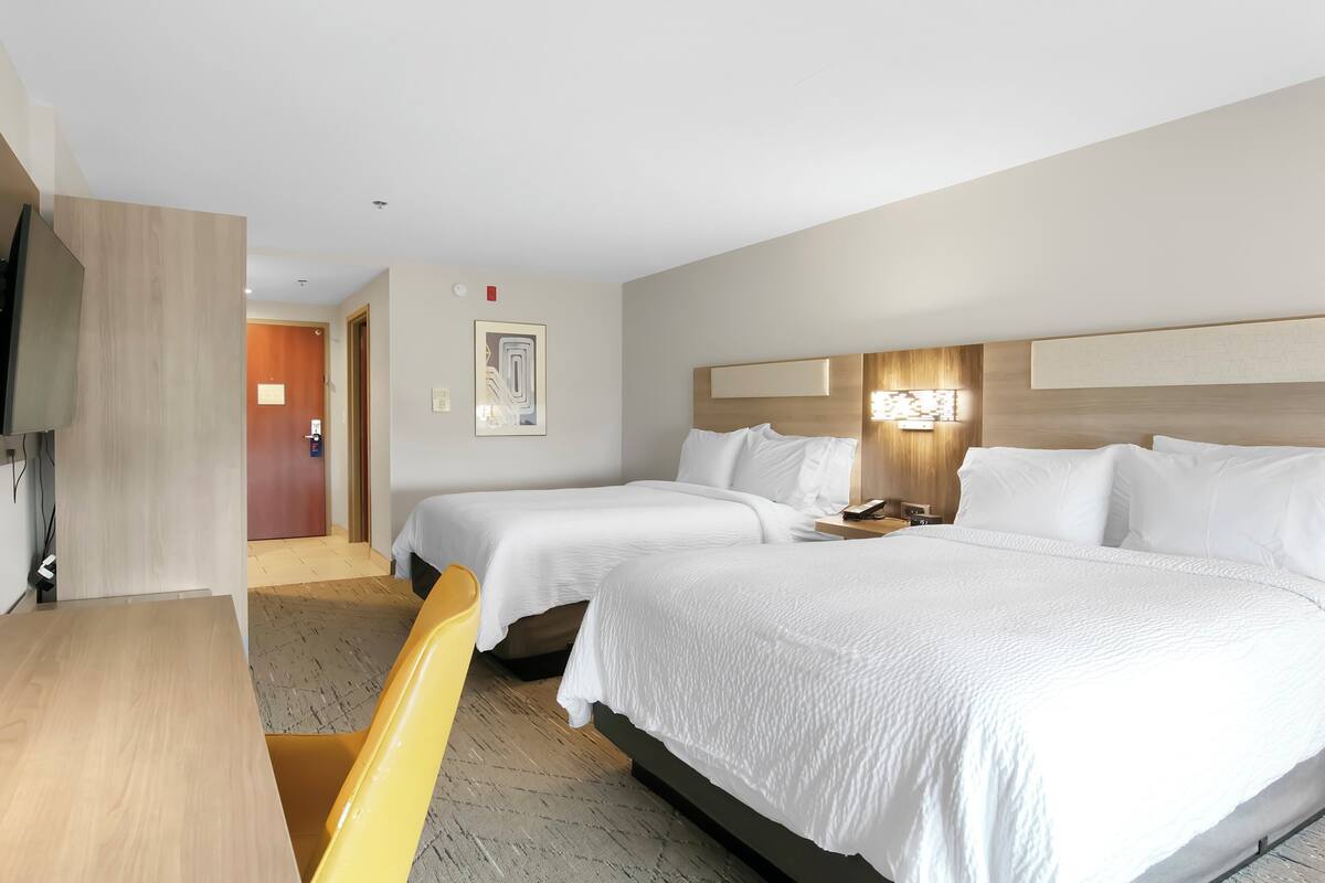 A hotel room with two single beds, a wooden desk, a chair, a TV, and a door leading to another room.