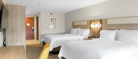 Habitación de hotel con dos camas individuales, un escritorio de madera, una silla, un televisor y una puerta que da a otra habitación.