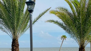 A balcony with two lounge chairs, a street lamp, and a view of the beach and ocean.