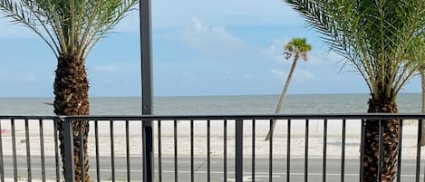 A balcony with two lounge chairs, a street lamp, and a view of the beach and ocean.