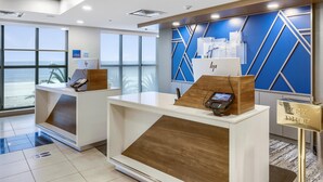 A hotel reception area with a view of the beach, a desk with a computer, and a sign for HP Holiday Inn Express.