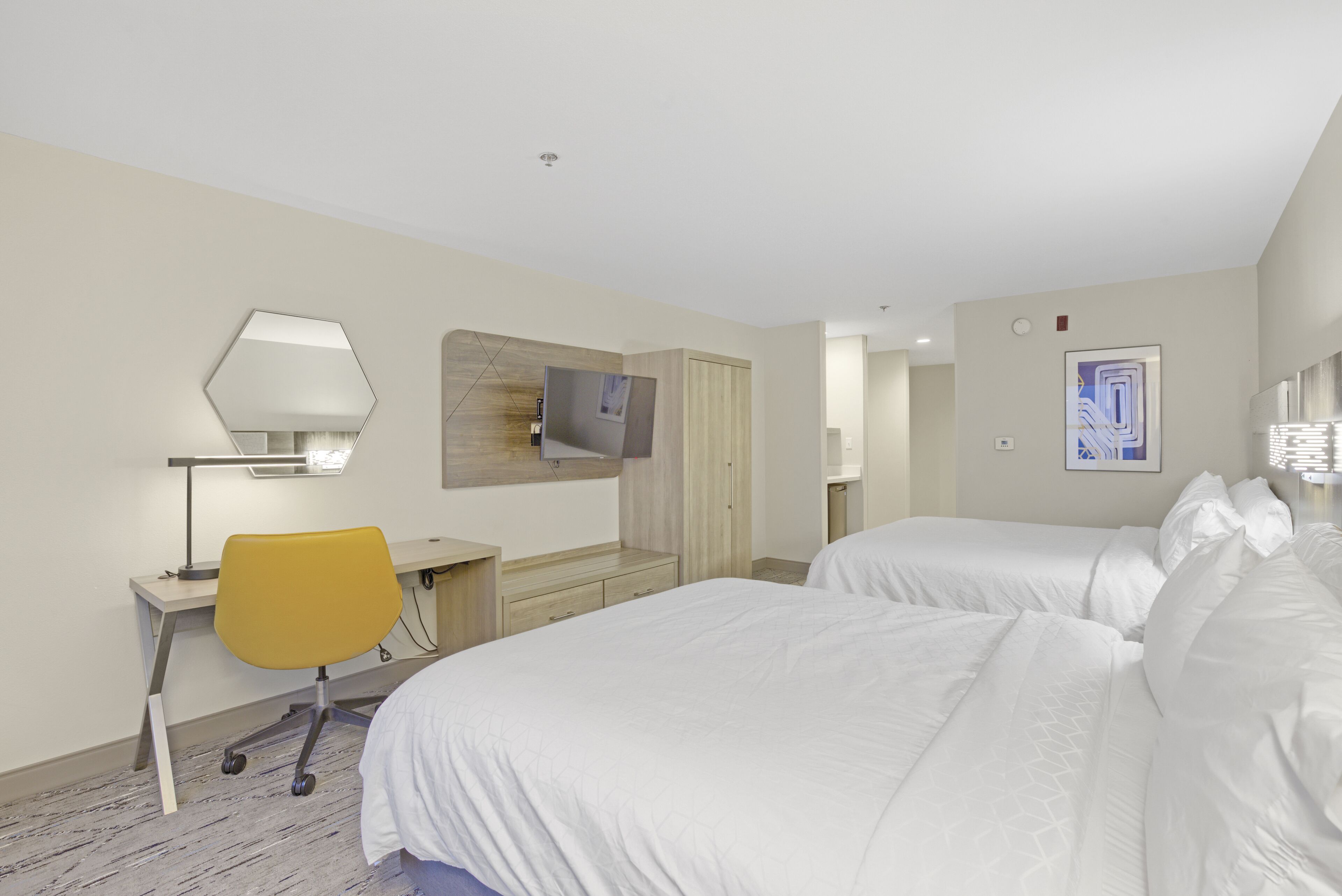 A hotel room with two beds, a desk with a chair, a TV mounted on the wall, and a wooden wardrobe.