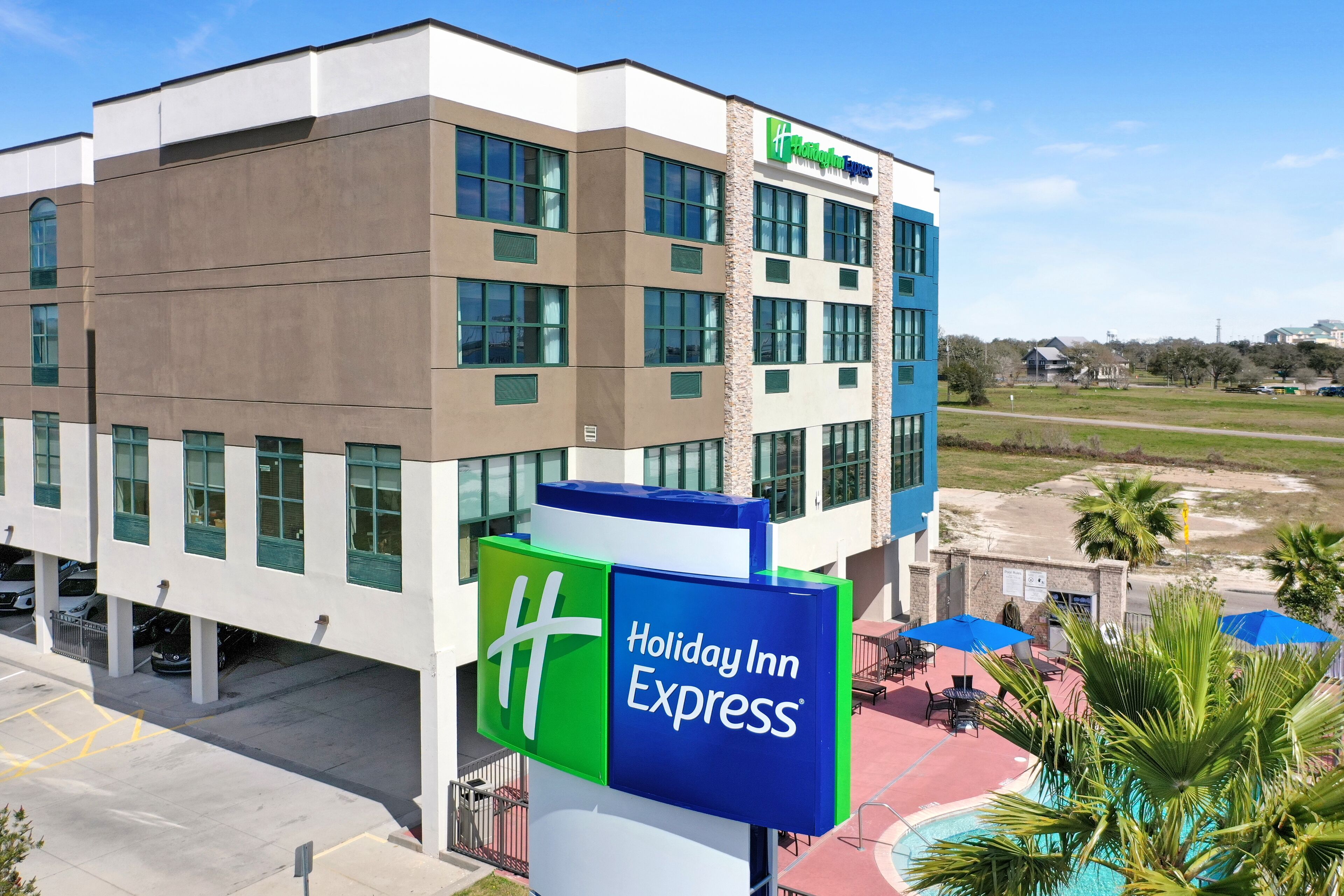 A Holiday Inn Express building with a clear view of the parking area and a pool with umbrellas.