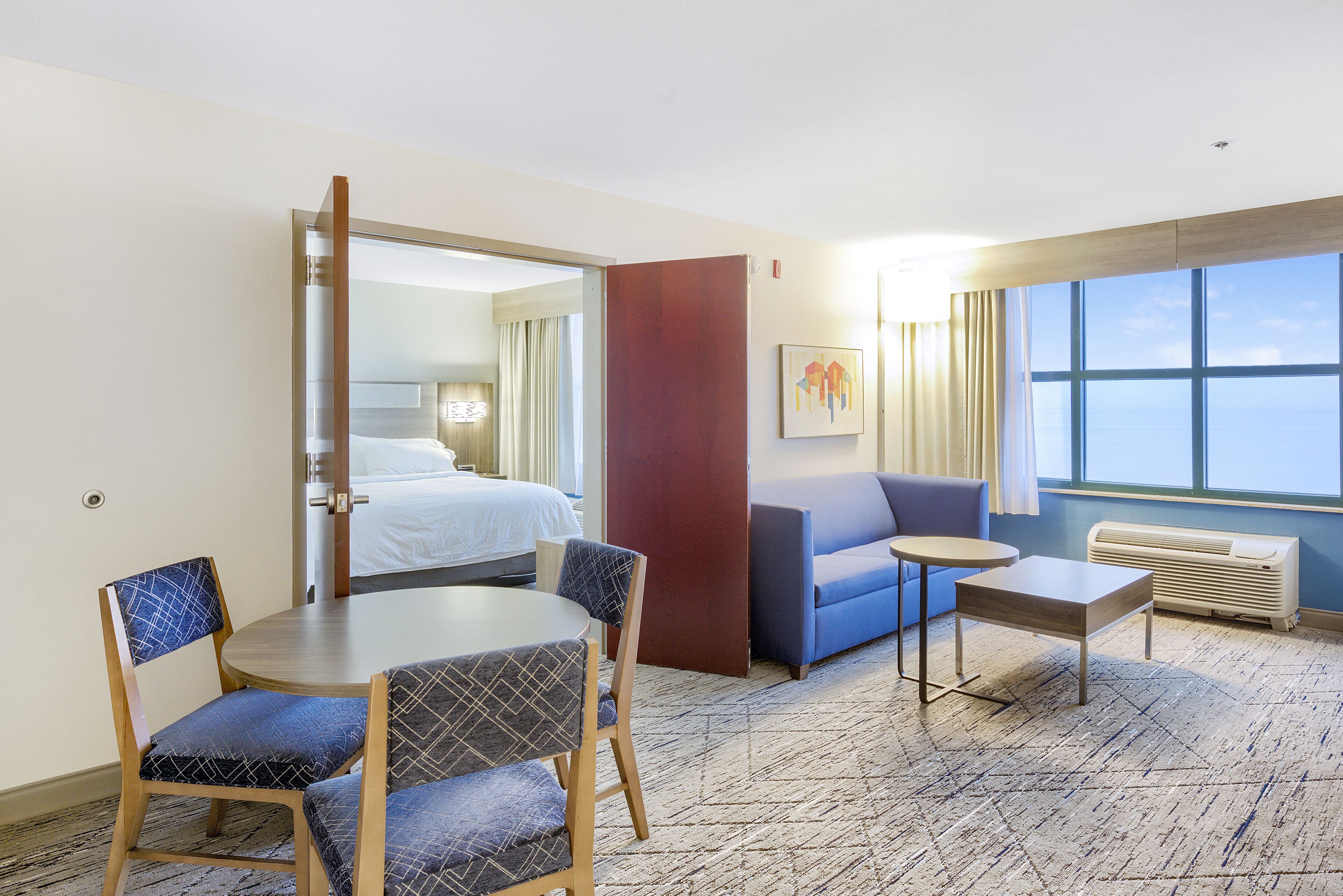 Een hotelkamer met een bed, een sofa, een eettafel met stoelen, een bijzettafeltje en een raam met uitzicht.