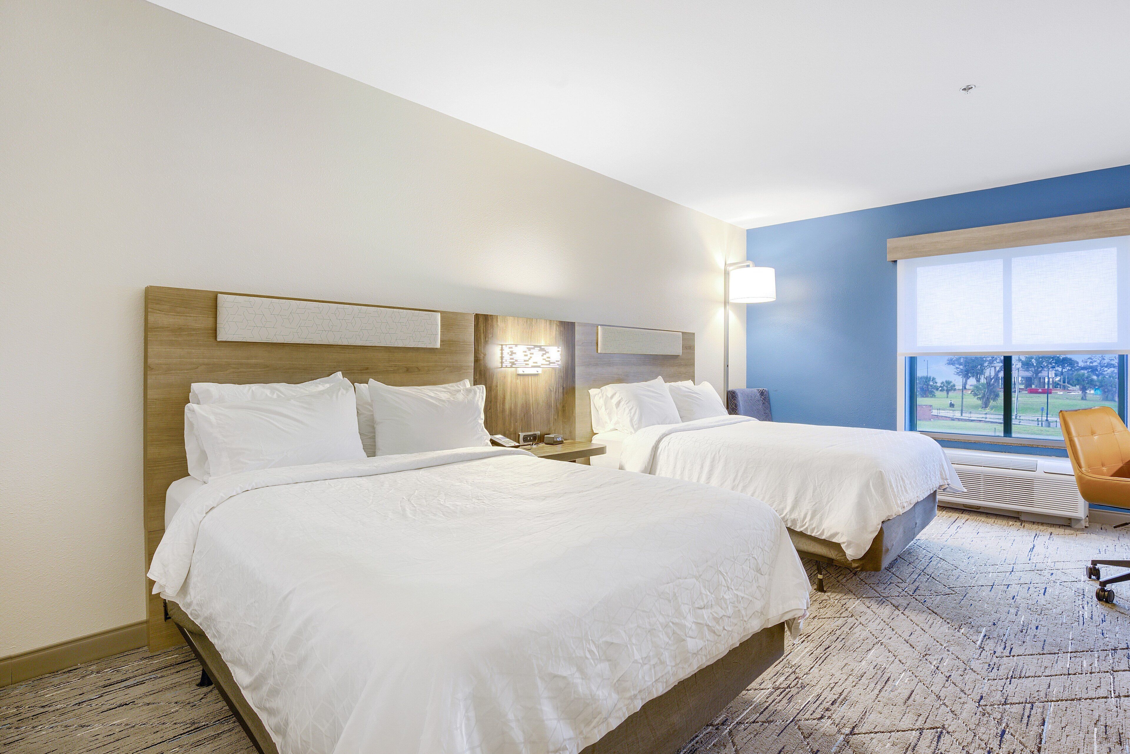 A hotel room with two beds, a large window, and a view of the outdoors.