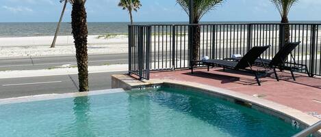 A pool with clear water, surrounded by palm trees and a beach view.