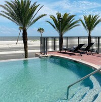 A pool with clear water, surrounded by palm trees and a beach view.