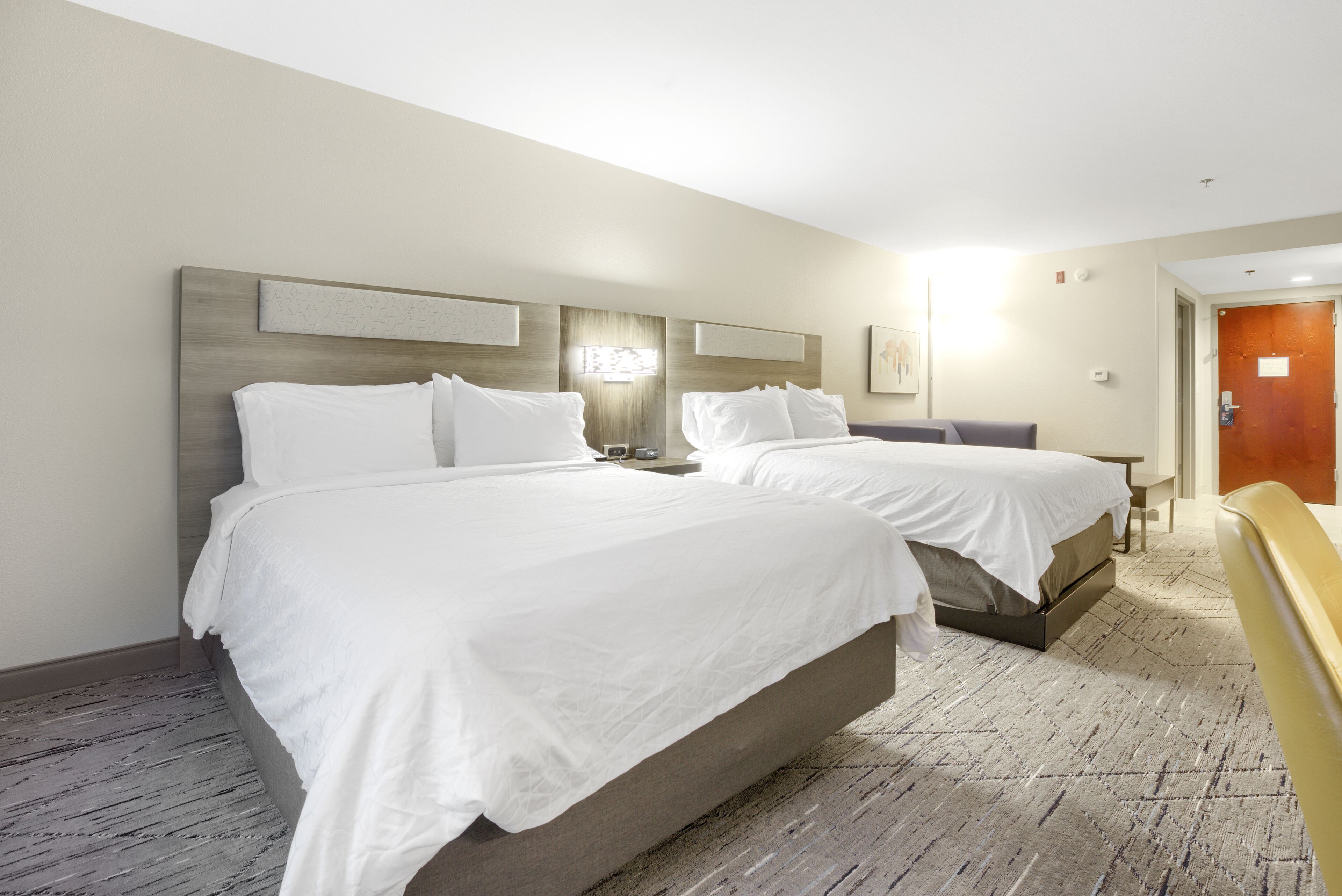 Habitación de hotel con dos camas, cabecero de madera, mesita de noche y escritorio con silla.
