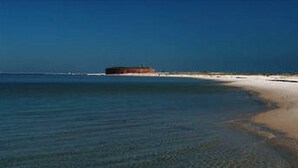 A beach with clear shallow waters leading to a sandy shore.