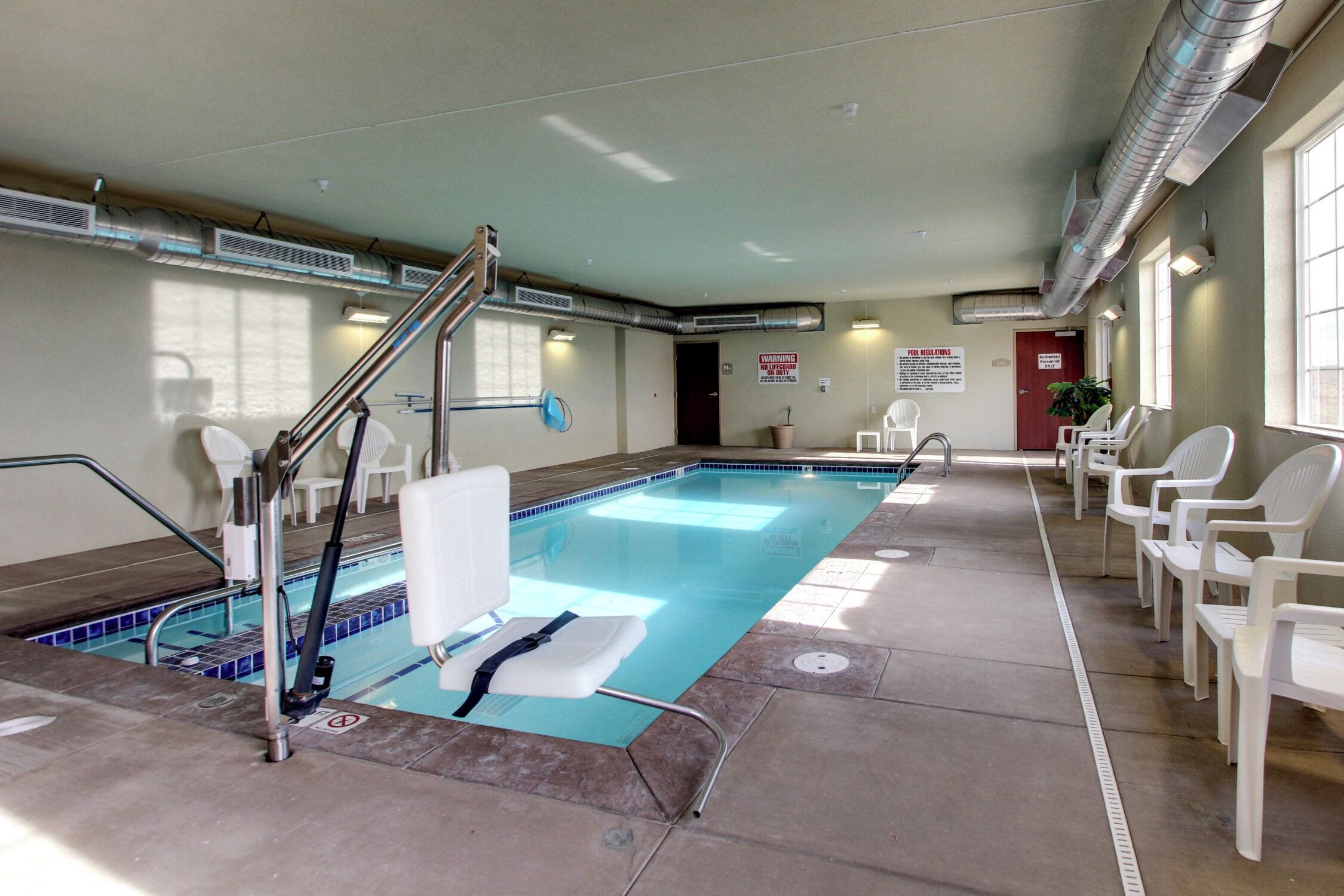 An indoor swimming pool with a lifeguard chair, a pool ladder, and a seating area with chairs.