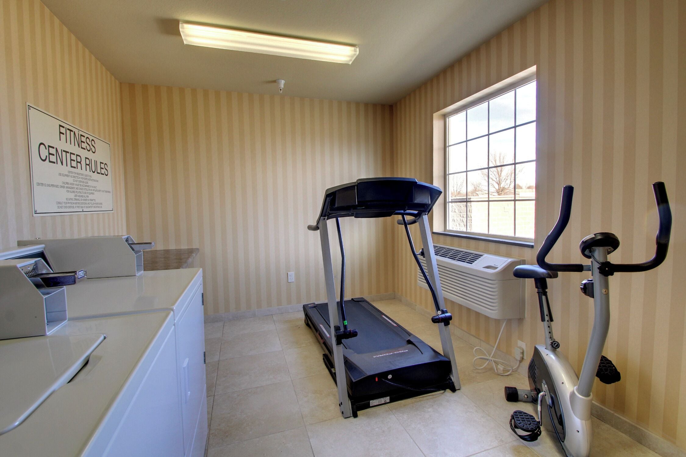 A fitness center with a treadmill, an exercise bike, and a wall-mounted air conditioning unit.