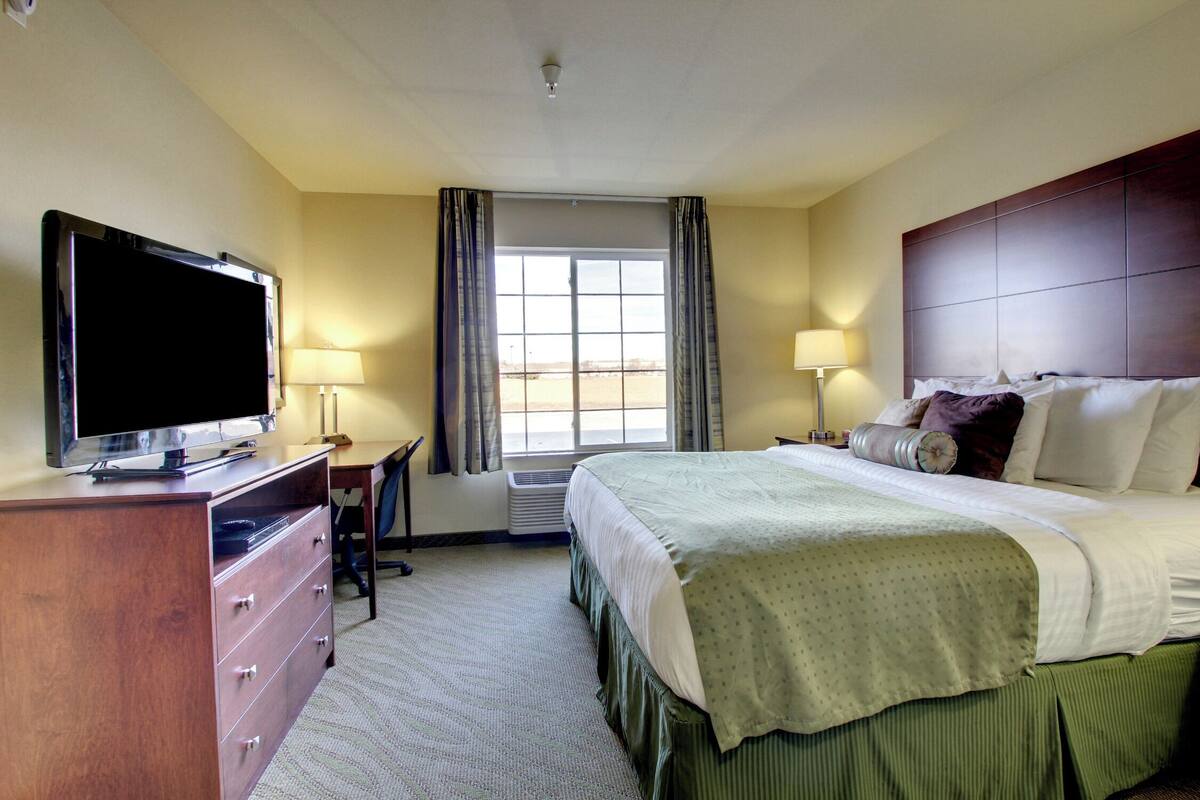 A hotel room with a bed, a TV, a desk, and a window with curtains.