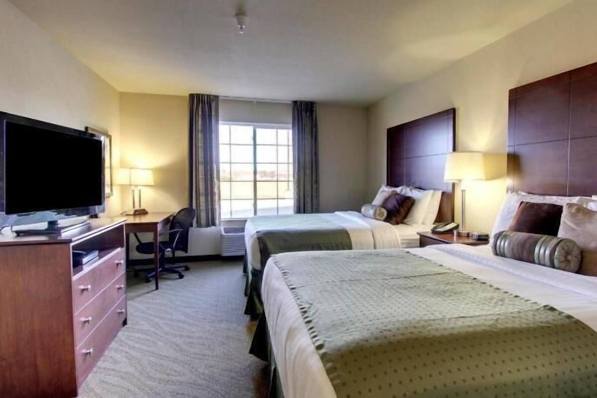 A hotel room with two beds, a TV, a desk, and a window.