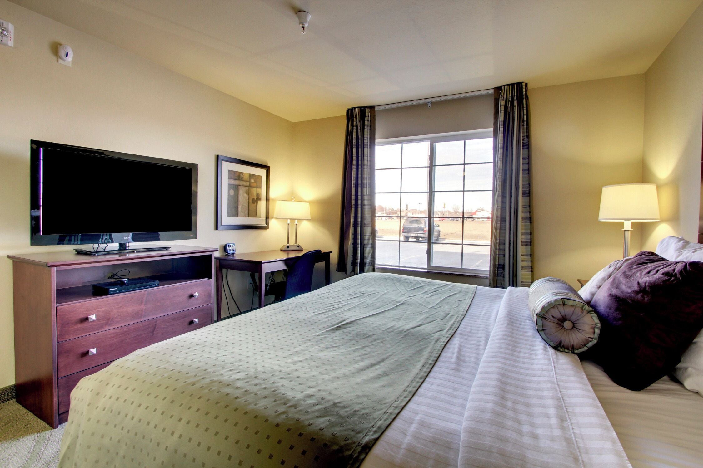 A hotel room with a bed, a desk, a television, and a window with curtains.