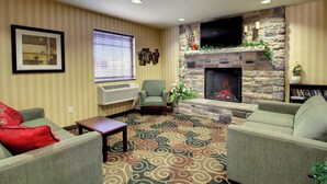 A living room with a fireplace, striped wallpaper, and a flat-screen TV mounted above it. - Cobblestone Hotel & Suites - Wayne (Wayne)
