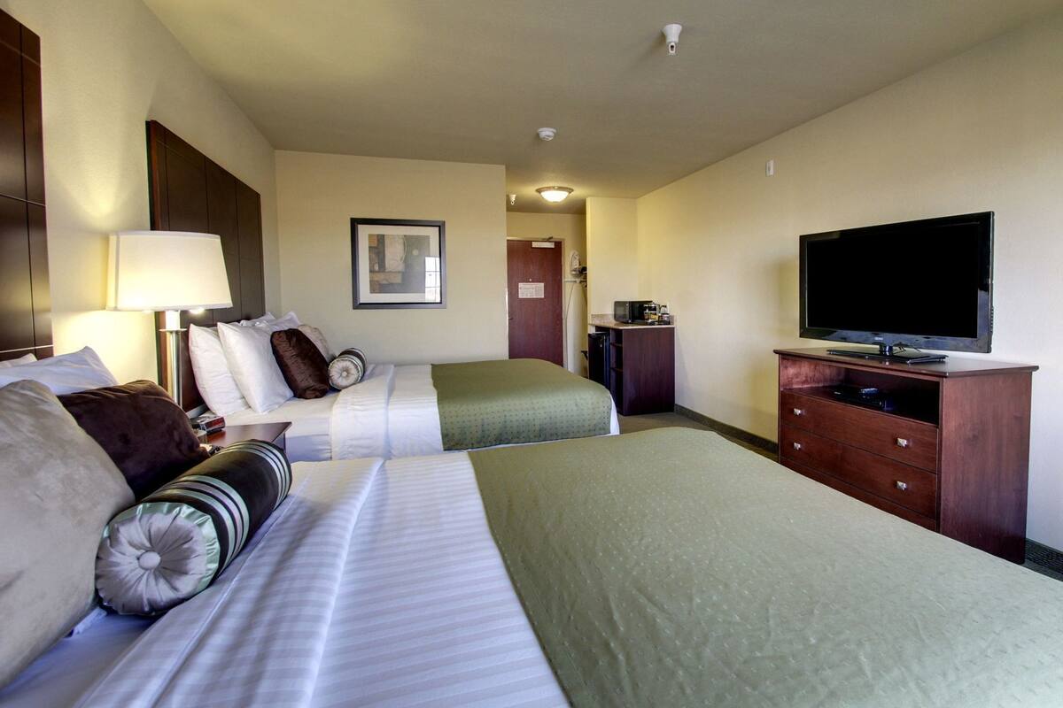 A hotel room with two beds, a television, a desk with a computer, and a door leading to a bathroom.