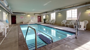 An indoor swimming pool with a tiled floor, a pool ladder, and white chairs around the pool area. - Cobblestone Hotel & Suites - Wayne (Wayne)