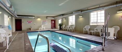 Una piscina interior con suelo de baldosas, una escalera de piscina y sillas blancas alrededor del área de la piscina.