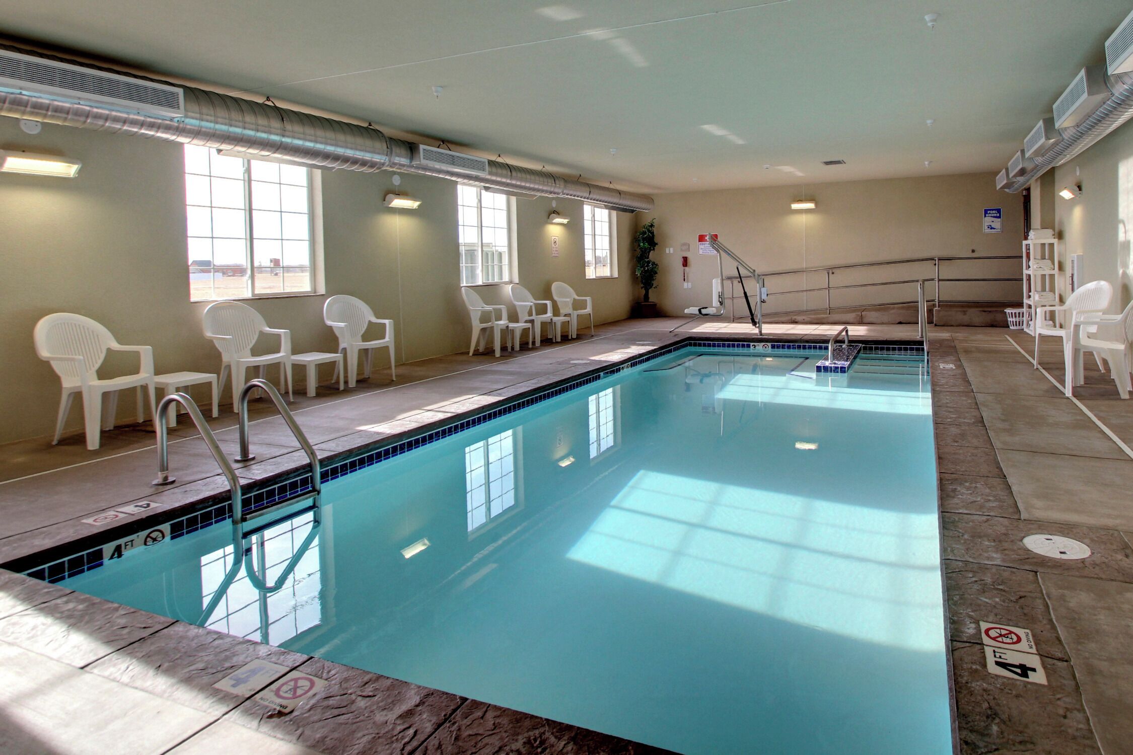 An indoor swimming pool with clear water, white chairs, and a sunlit room.