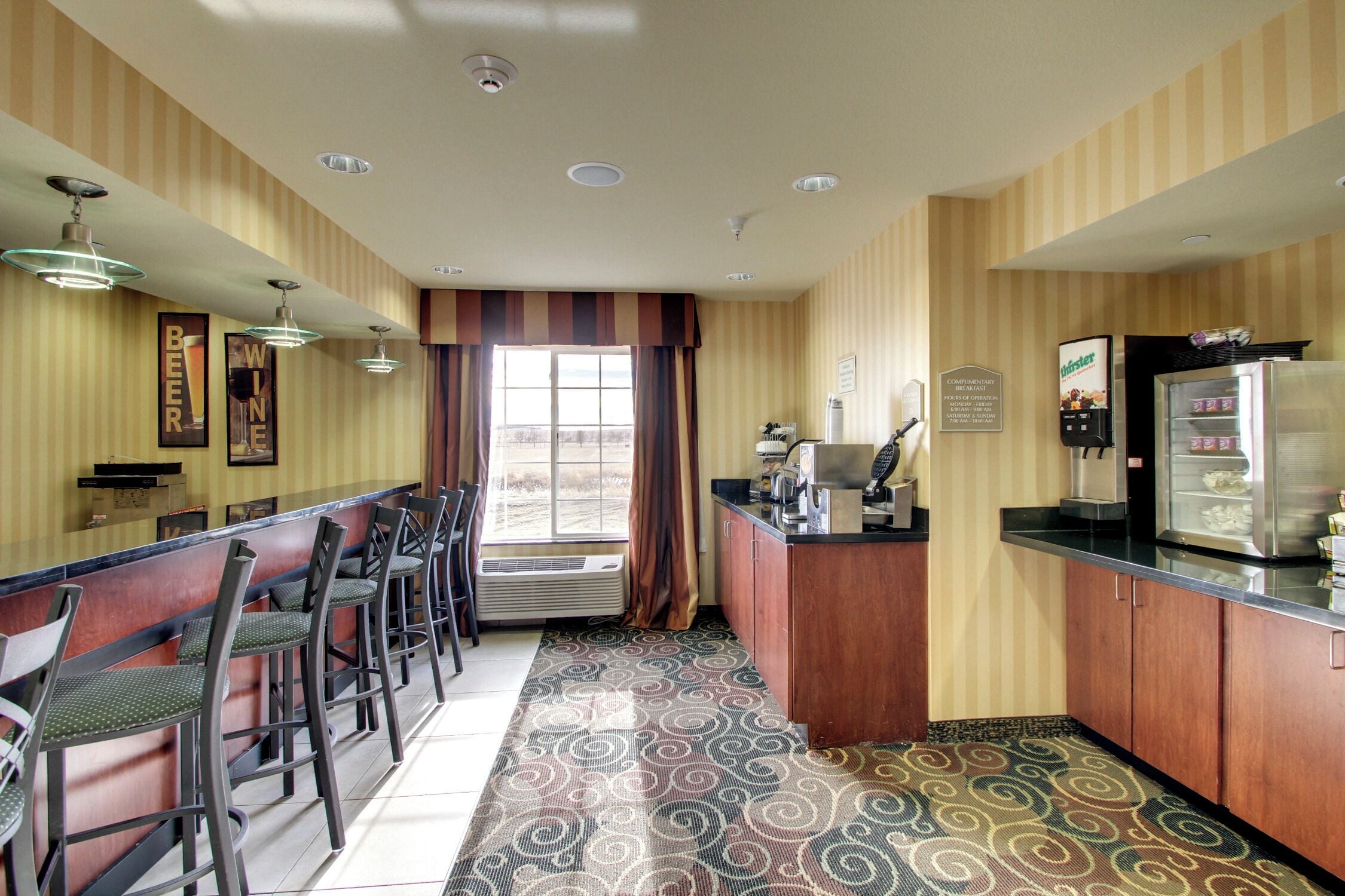 A hotel bar with striped wallpaper, a patterned carpet, and a window with curtains.
