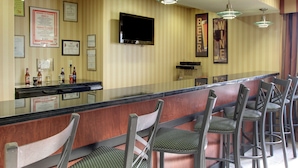 A bar area with a counter, bar stools, a television mounted on the wall, and framed certificates on the wall. - Cobblestone Hotel & Suites - Wayne (Wayne)