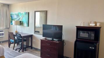 Una habitación de hotel con cama, escritorio, silla, televisor, espejo y microondas.