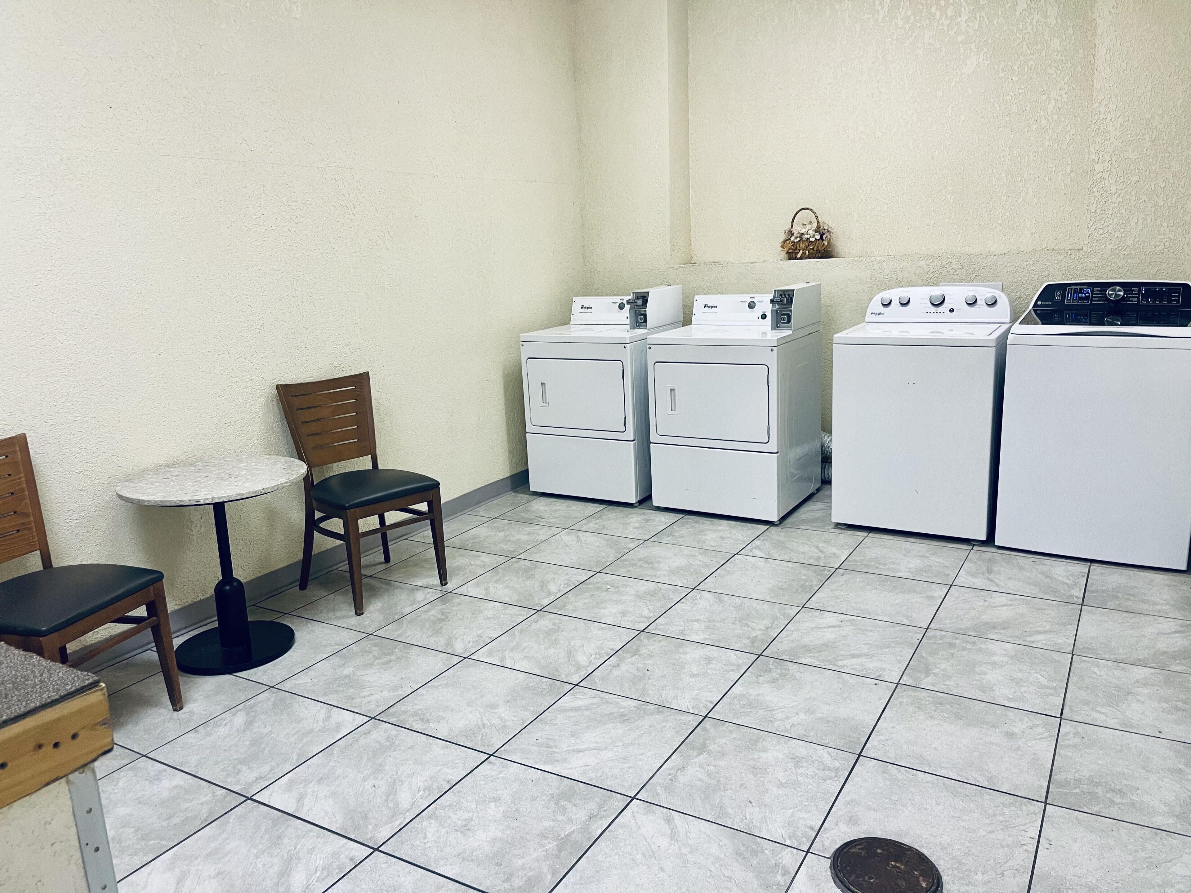 A compact laundry room with a small table and two chairs, three stacked washing machines, and a tiled floor.
