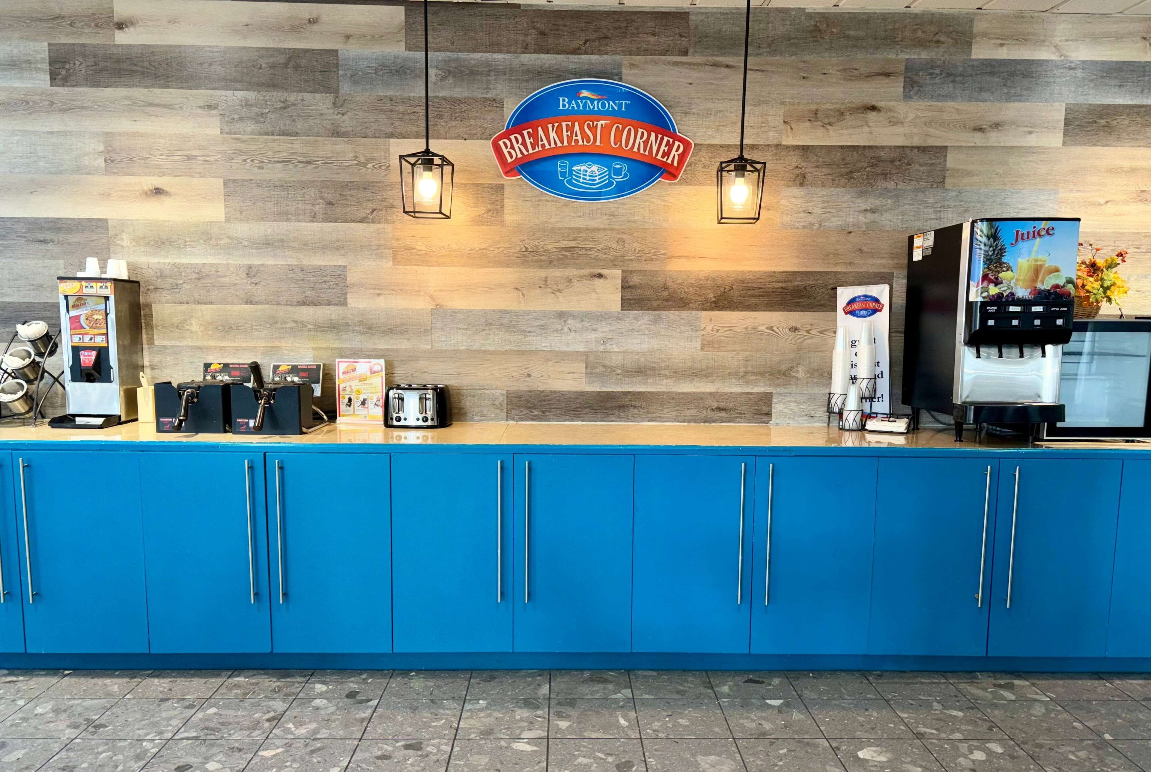 Ein Frühstücksbuffet mit Holzwand, blauem Schrank, einer Kaffeemaschine und einem Saftspender.