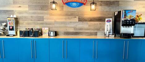 Ein Frühstücksbuffet mit Holzwand, blauem Schrank, einer Kaffeemaschine und einem Saftspender.