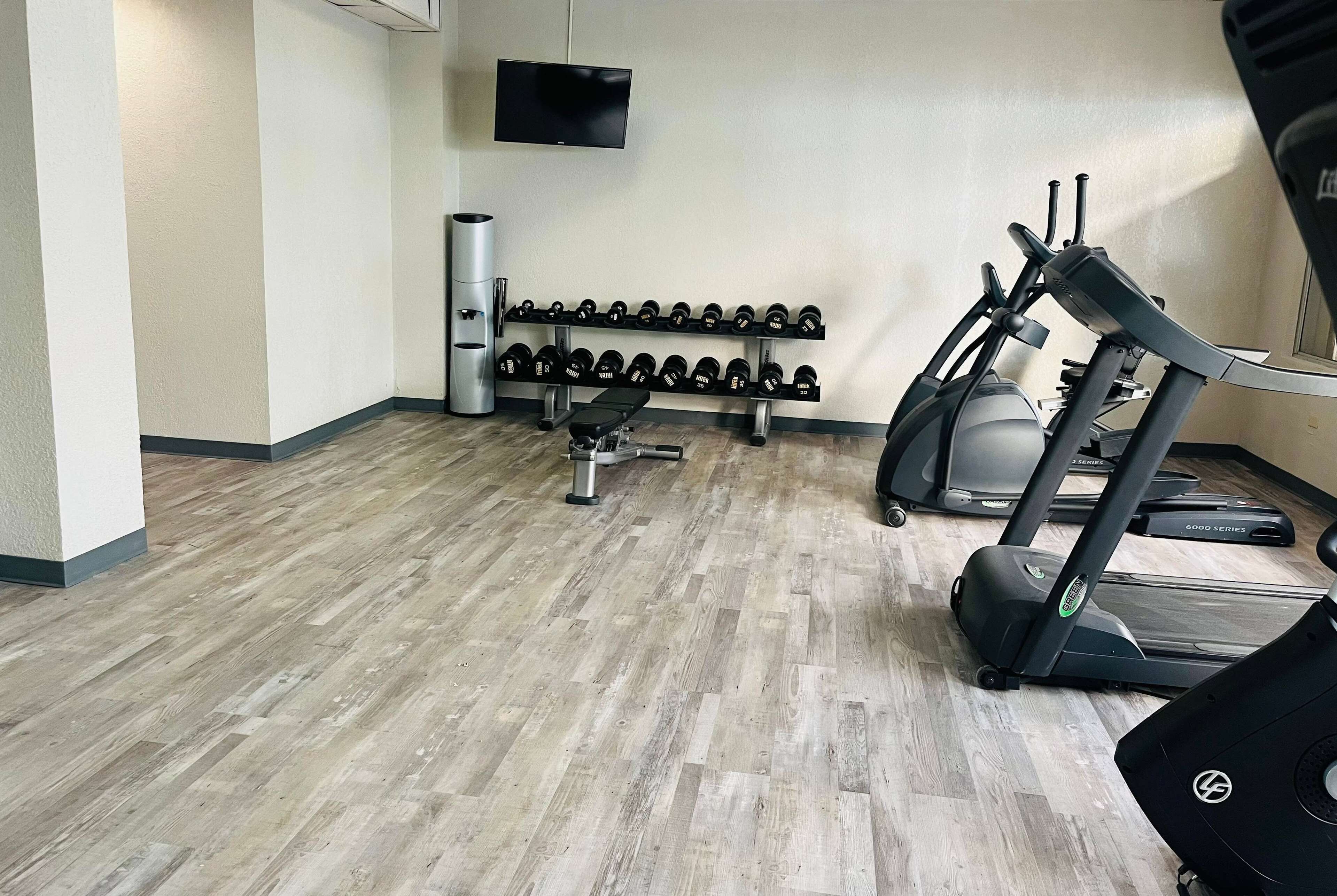 Ein Fitnessstudio mit Laufbändern, Hanteln und einer Bank.