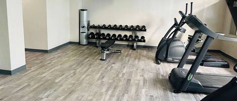 Ein Fitnessstudio mit Laufbändern, Hanteln und einer Bank.