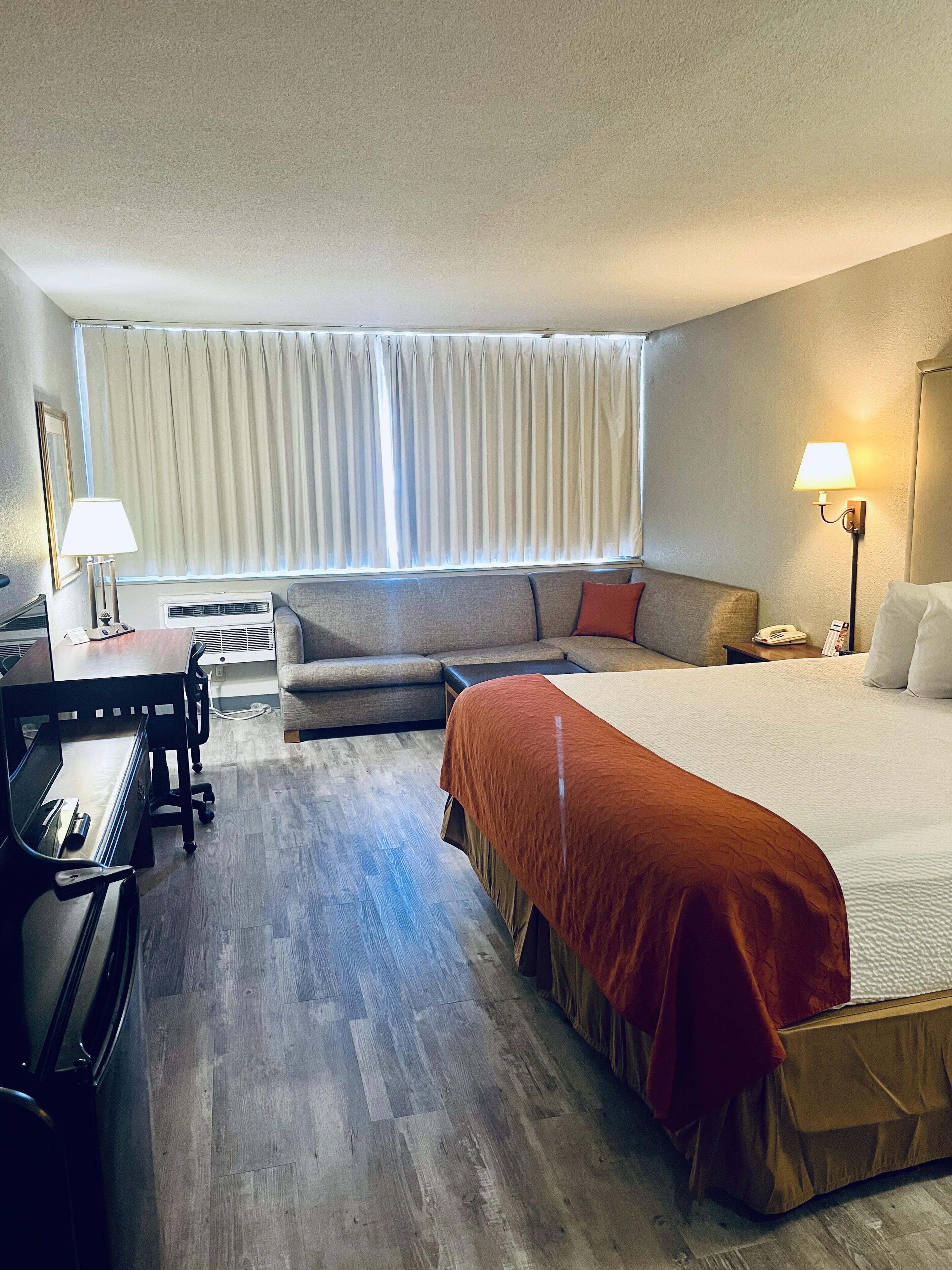 Una habitación de hotel con cama, sofá, escritorio con lámpara y piano.