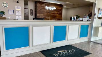A reception desk with a wooden back panel and a neon sign that reads "Baymont."