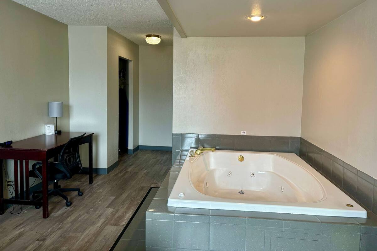 Ein Hotelzimmer mit einer großen Badewanne, einem Schreibtisch mit Stuhl und einer Lampe.