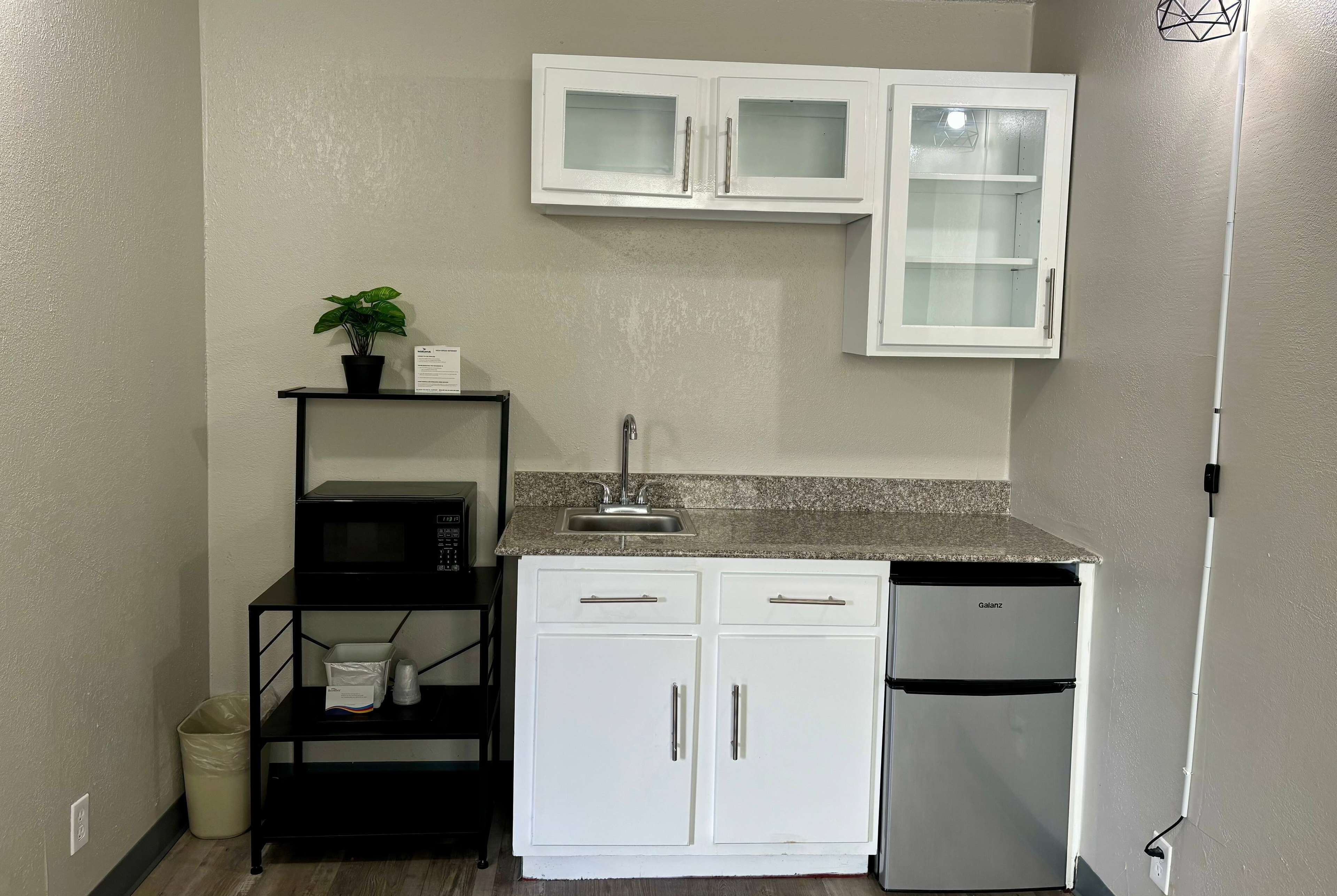 A compact kitchen with white cabinets, a microwave, a sink, and a refrigerator.