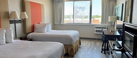 Habitación de hotel con dos camas, un escritorio con computadora, un televisor y una ventana con cortinas.