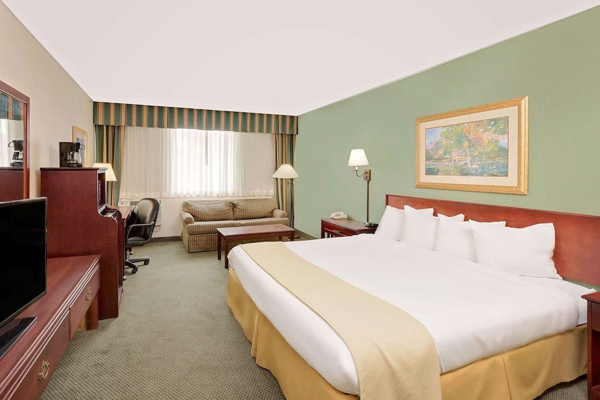Ein Hotelzimmer mit einem großen Bett, einer Couch, einem Schreibtisch mit Computer, einem Fernseher und einem Bild an der Wand.