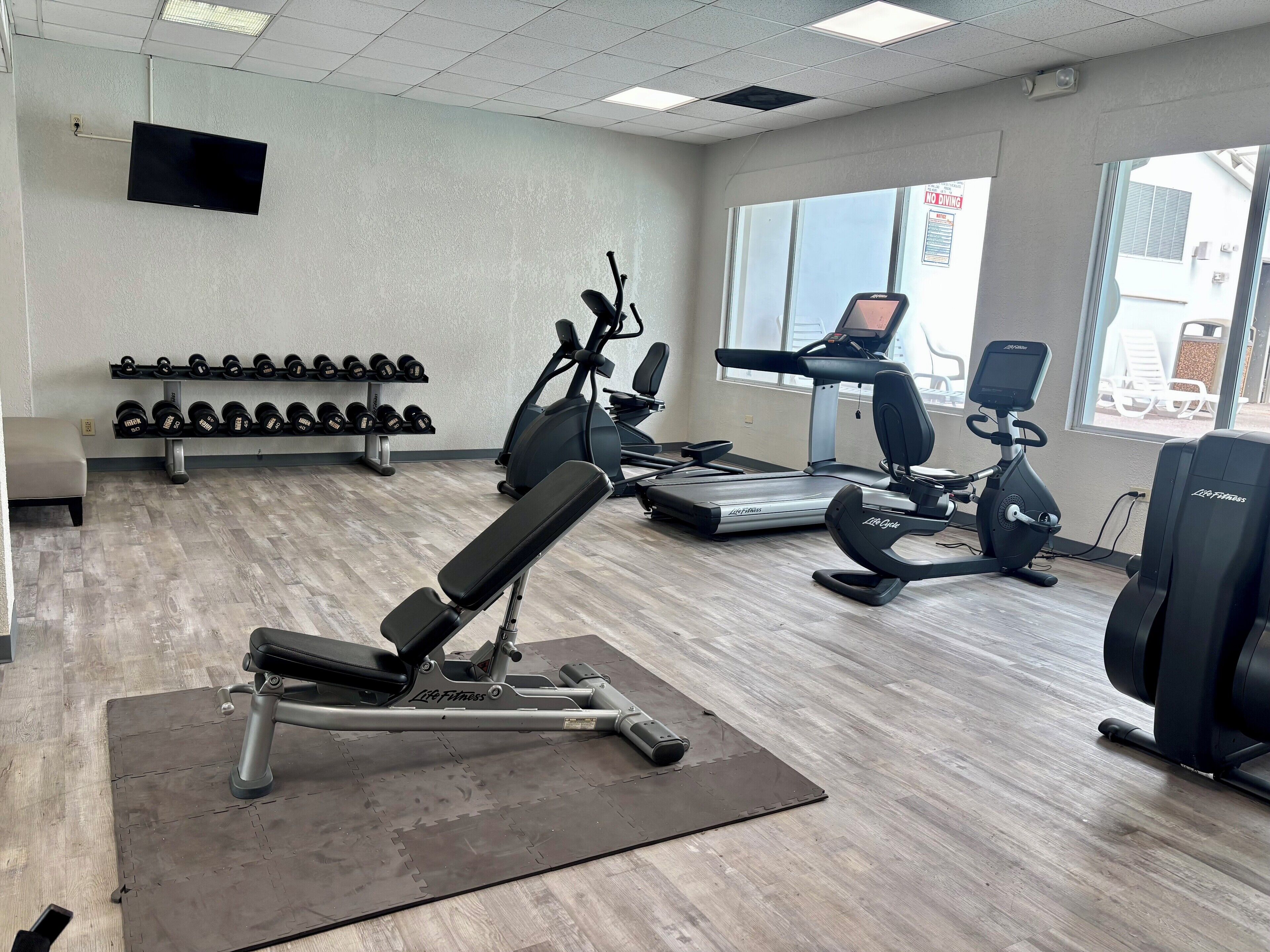 Une salle de sport équipée de machines de cardio, d’haltères et d’un banc de musculation.