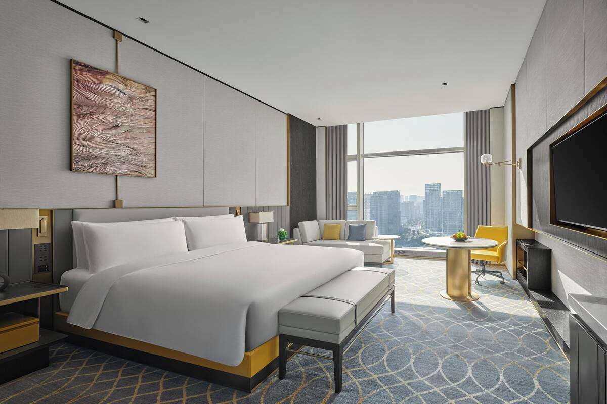 Habitación de hotel moderna con una cama grande, un escritorio, una silla, una mesita, un televisor y vistas a la ciudad.