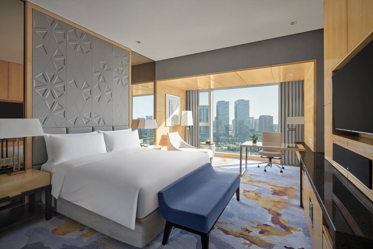 Una habitación de hotel moderna con una cama grande, un escritorio, un televisor y vistas a la ciudad.