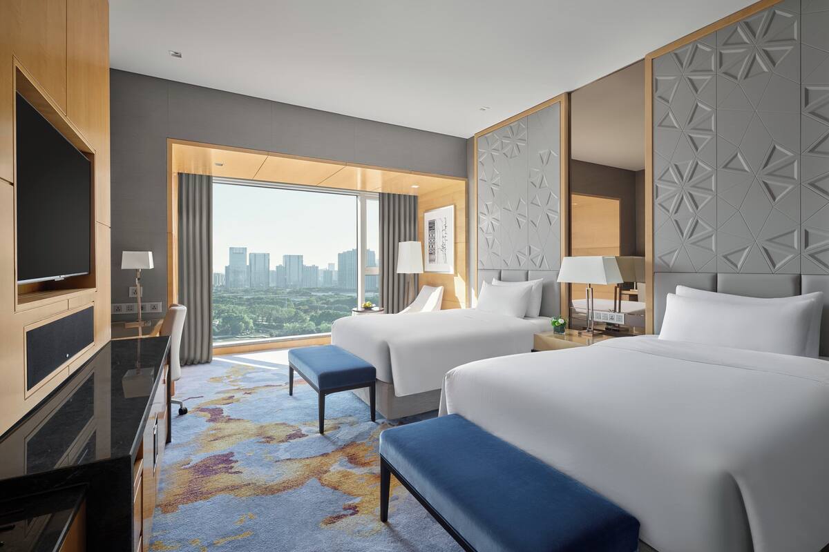 Habitación de hotel con dos camas, un televisor y un ventanal amplio que ofrece vistas a la ciudad.