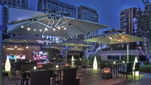 An outdoor patio area with tables and chairs, large umbrellas, string lights, and a neon sign in the background. - The Azure Ningbo, Vignette Collection by IHG (Ningbo)