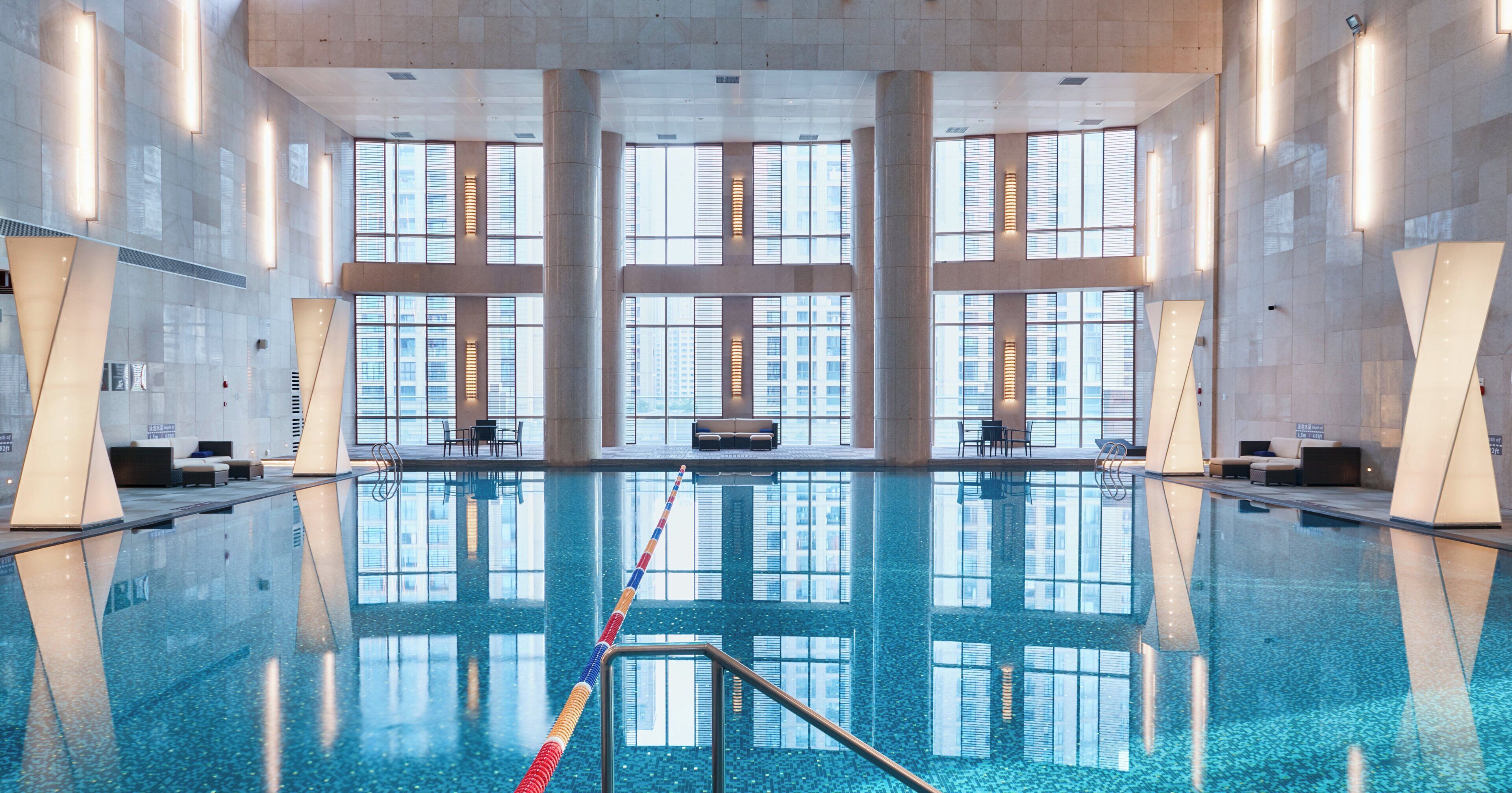 A large indoor swimming pool with clear water, surrounded by seating areas and large windows.