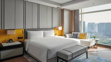 A modern hotel room with a large bed, a bench, a sofa, and a view of the city.