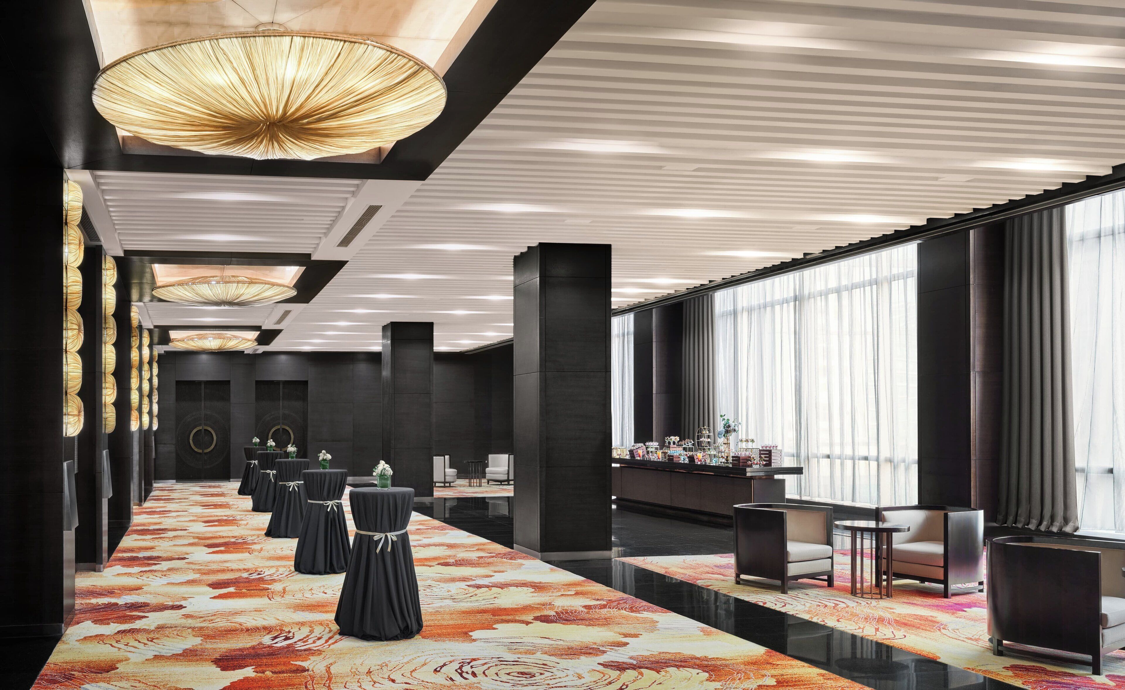 A modern hotel lobby with a long reception desk, black chairs, and a patterned carpet.