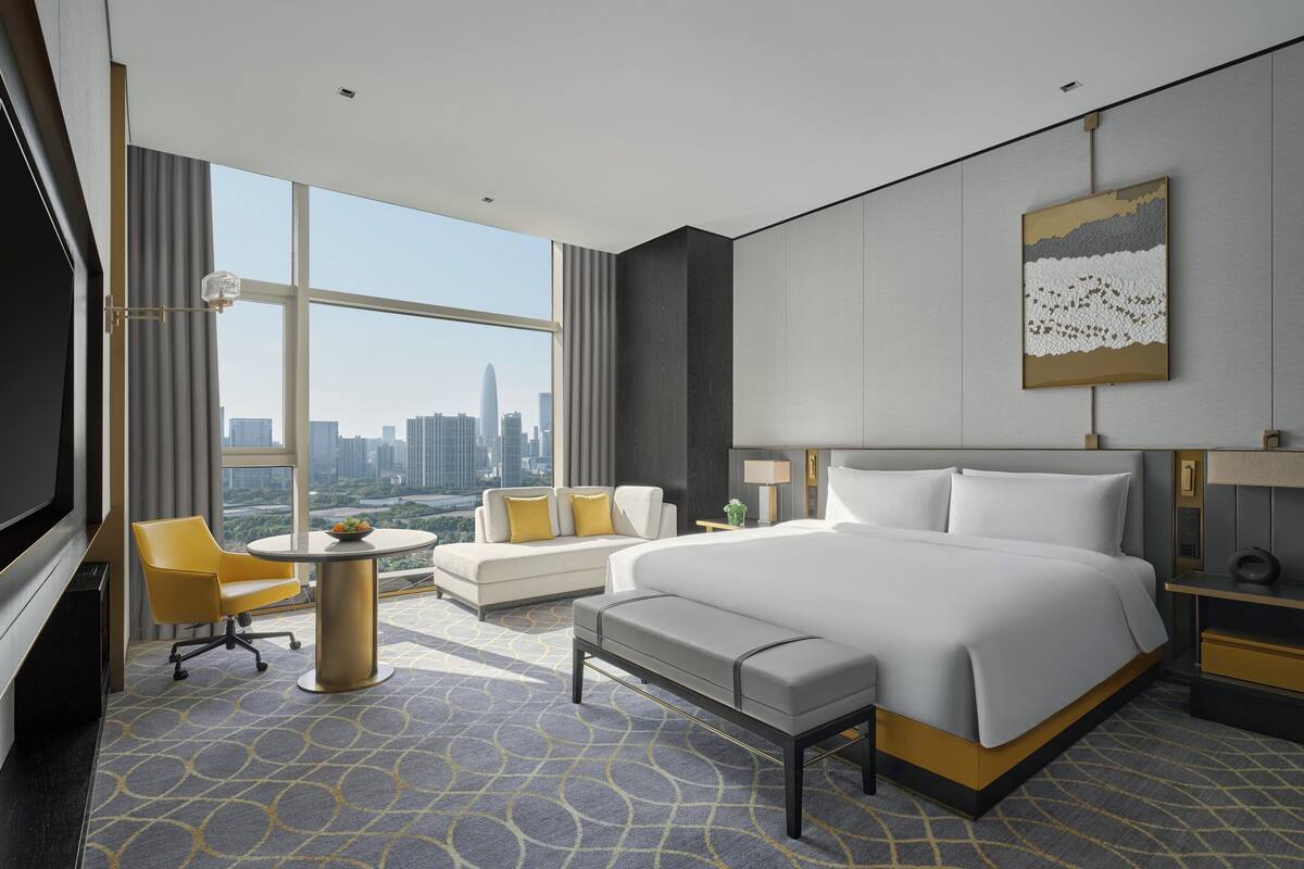 Habitación de hotel moderna con una cama grande, un sofá, un escritorio y vistas al horizonte de la ciudad.