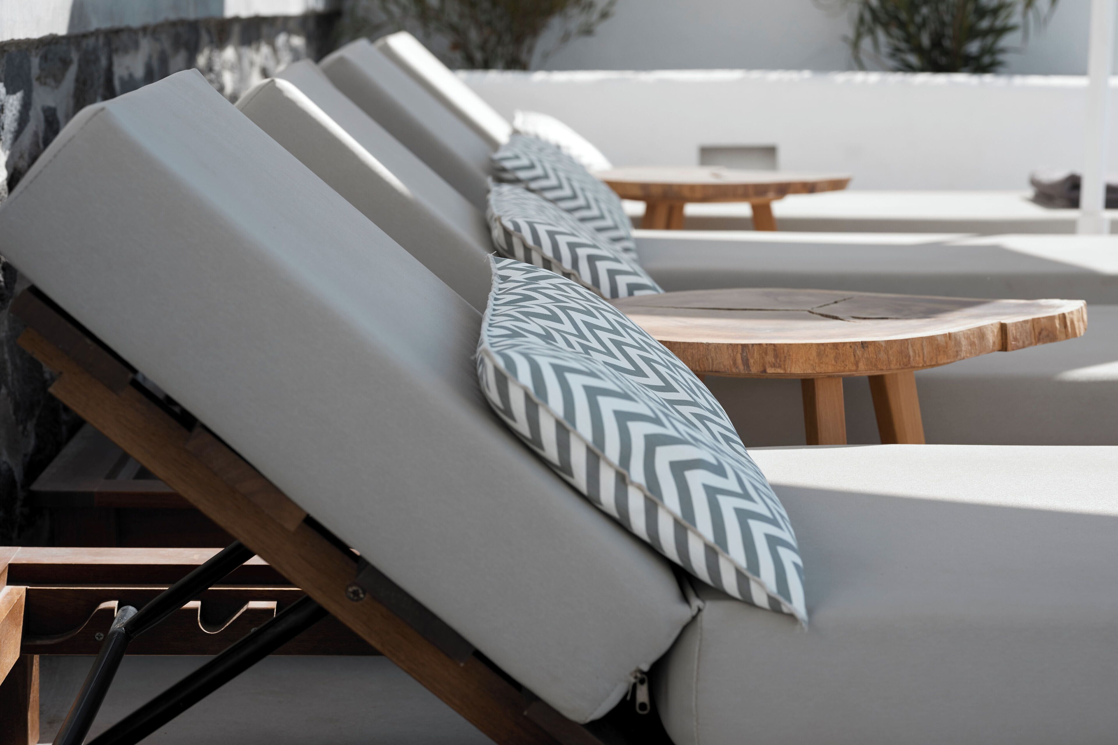 Une rangée de chaises longues avec des coussins à motifs, une table en bois et un mur blanc en arrière-plan.