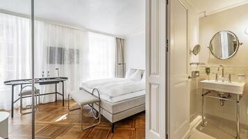 A hotel room with a bed, a desk, and a bathroom with a sink and mirror.