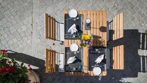 An outdoor dining area with a wooden table set for four, surrounded by chairs, on a paved surface. - BLUME. - Baden Hotel & Restaurant (Baden)